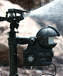 A close-up image of an activated water sprinkler system in a garden. Water sprays out forcefully from the nozzle, creating a mist around the sprinkler. The background is blurred, drawing focus to the sprinkler's robust and detailed mechanism—an effective choice when comparing deer repellent spray vs mechanical control.
