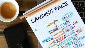 A notebook page titled "Landing Page" with a hand-drawn wireframe for a webpage design is placed on a laptop keyboard. A pencil rests across the notebook, alongside a smartphone displaying "10:16" and a small cup of coffee. A notebook page titled "Landing Page" with a hand-drawn wireframe for a webpage design is placed on a laptop keyboard. A pencil rests across the notebook, alongside a smartphone displaying "10:16" and a small cup of coffee.